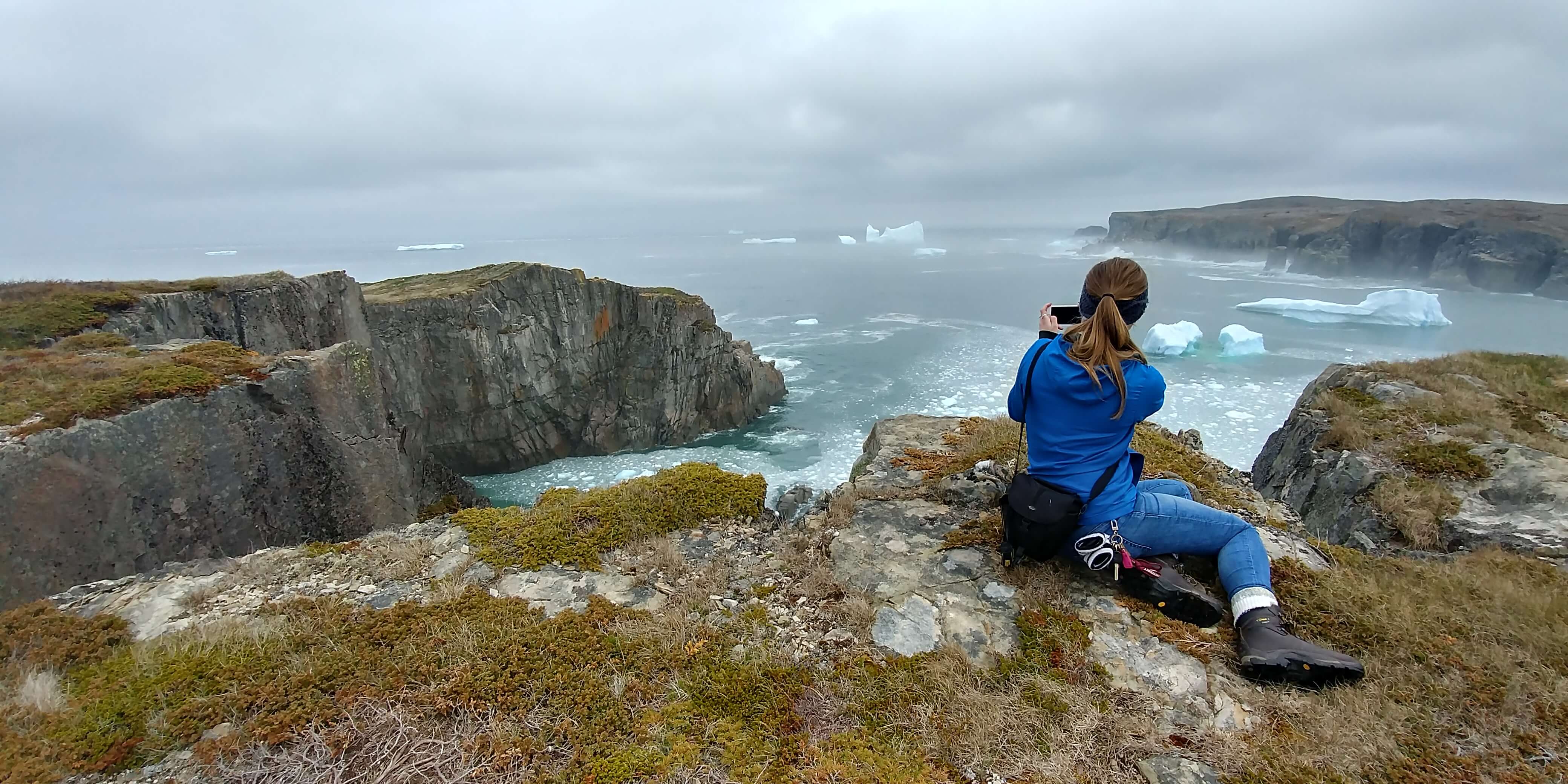 a woman takes a photo of cliffs and icebergs from the Klondike Trail