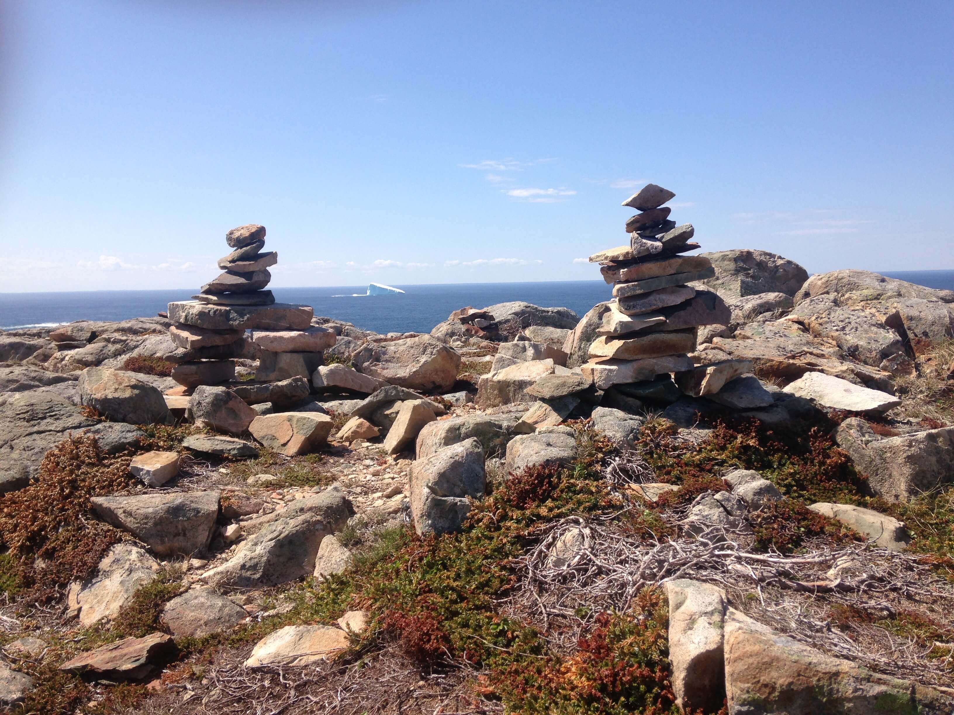 2 piles of rocks lie on either side of the picture with a view of an iceberg in the ocean between them.