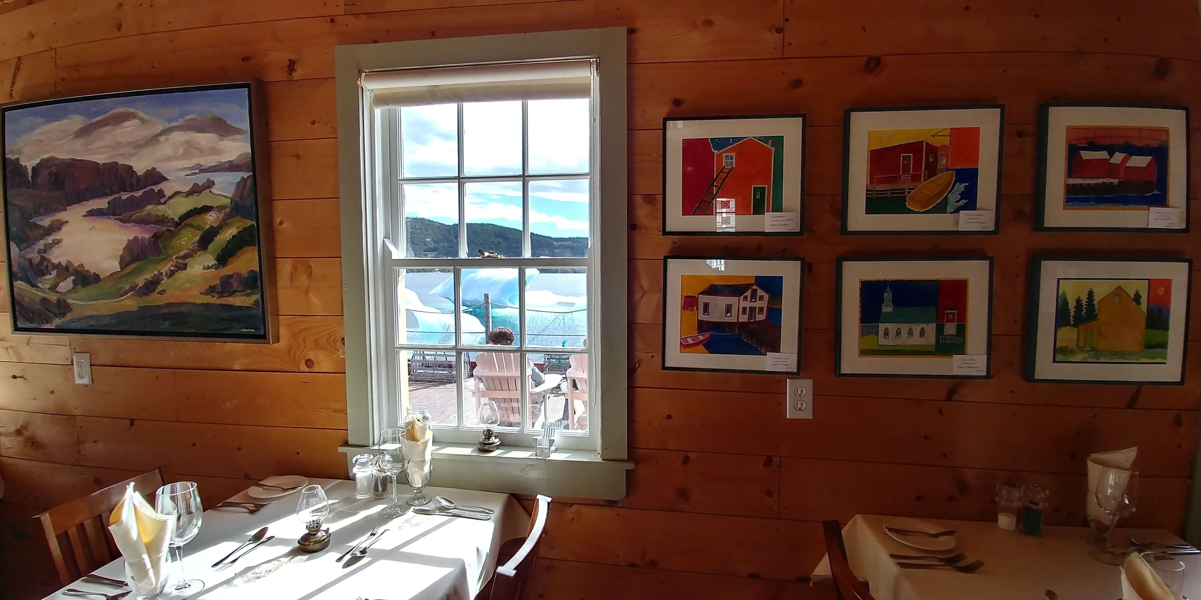 Artwork is displayed on wooden walls adjacent to a window in a dining room