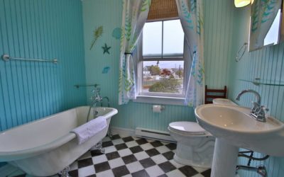 Clawfoot bathtub, checkered floor, toilet and pedestal sink with a window overlooking the town