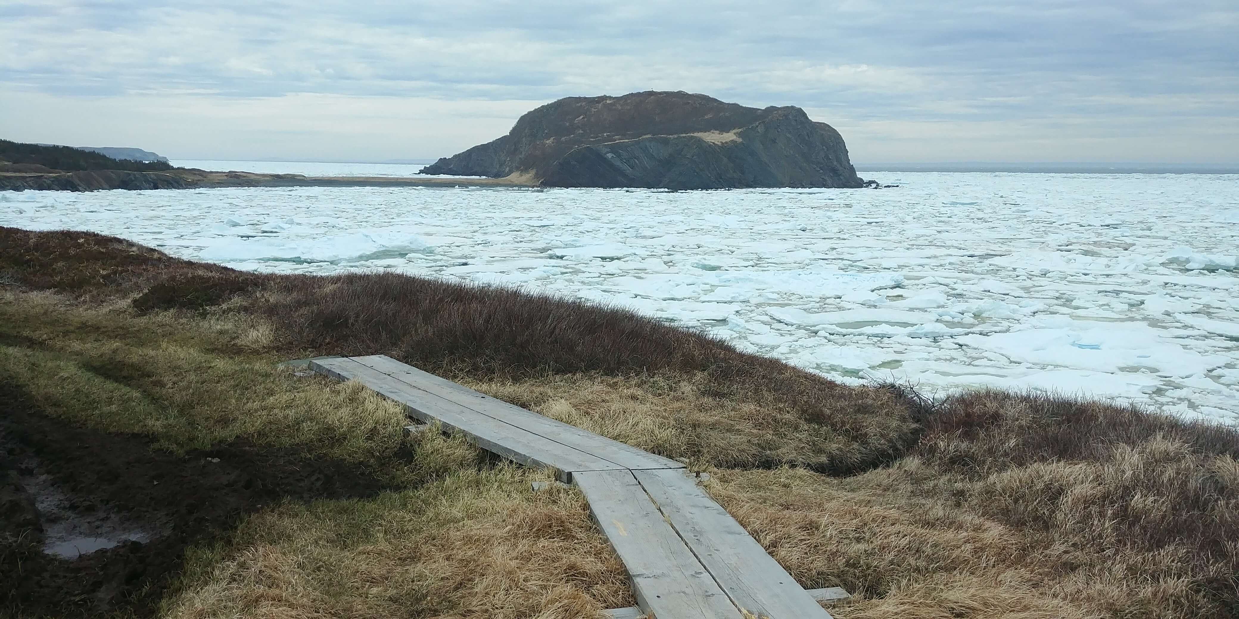 A board walk along the ocean overlooking fox island encircled by pack ice