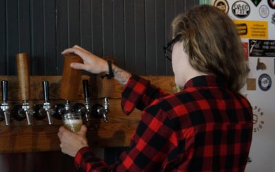 A girl in a plaid shirt pulls a pint of beer