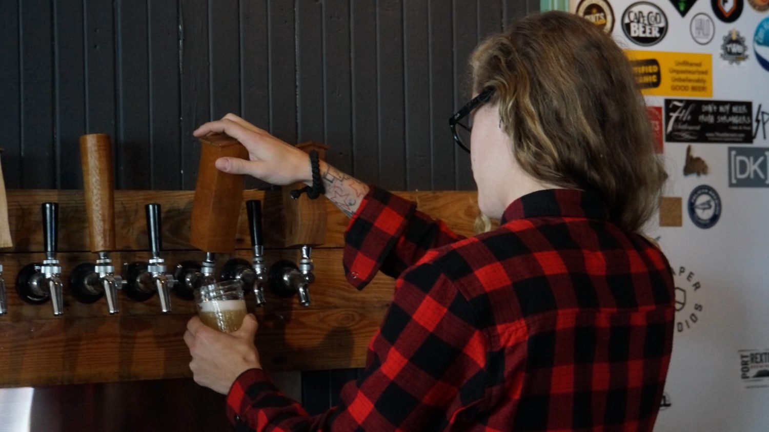 A girl in a plaid shirt pulls a pint of beer