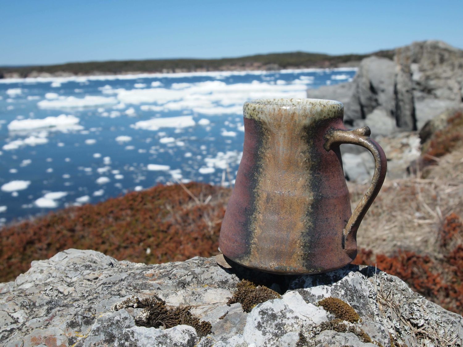 A clay mug sits on a rocky coastline with pack ice in the background